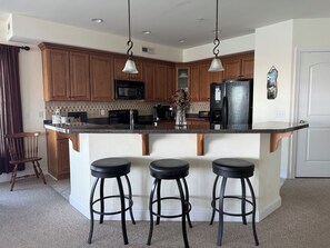 A kitchen with wooden cabinets, a black refrigerator, a microwave, and a bar stool area.