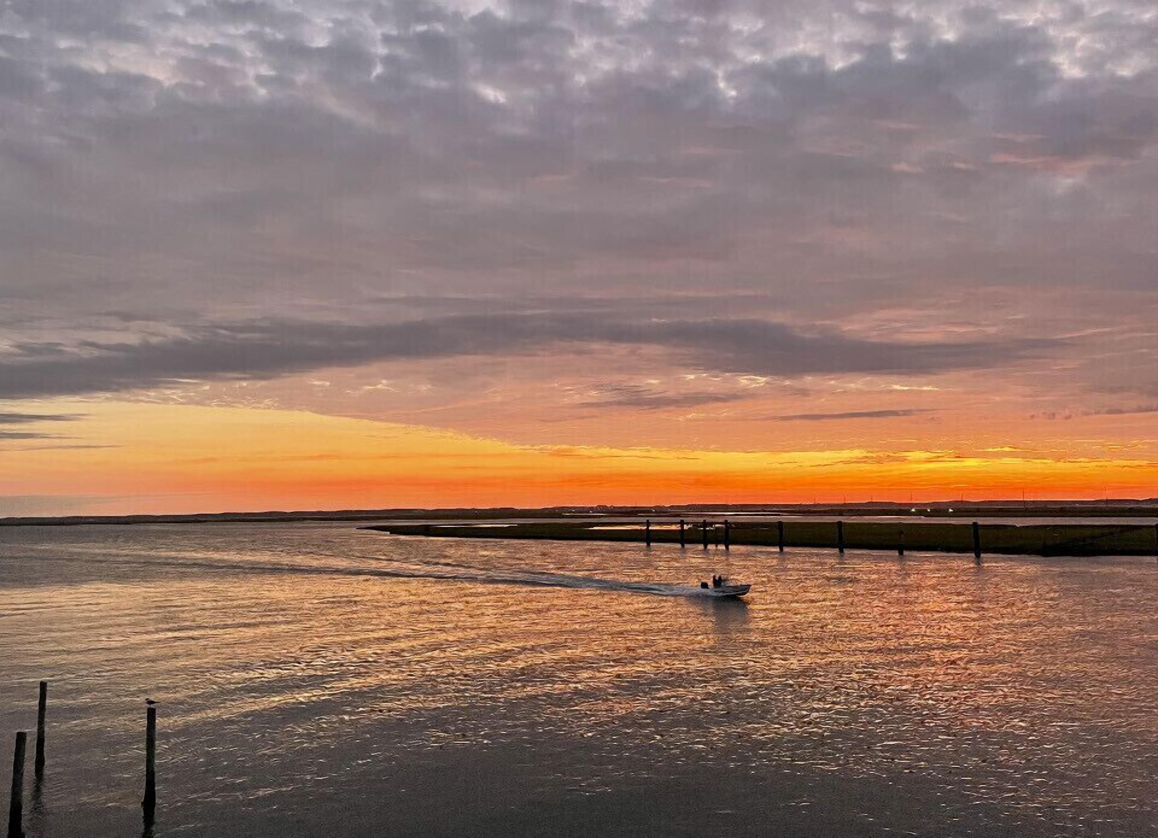 Un coucher de soleil sur une étendue d’eau calme, avec un bateau en mouvement.