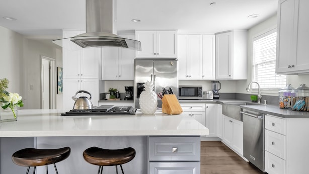 Una cocina moderna con armarios blancos, electrodomésticos de acero inoxidable y una isla central con taburetes.