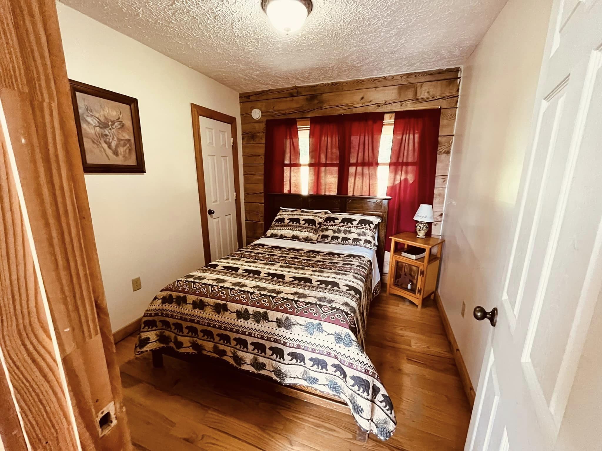 Quarto com cabeceira de madeira, cama com roupa de cama estampada, mesa de cabeceira com abajur e porta com pequena janela.
