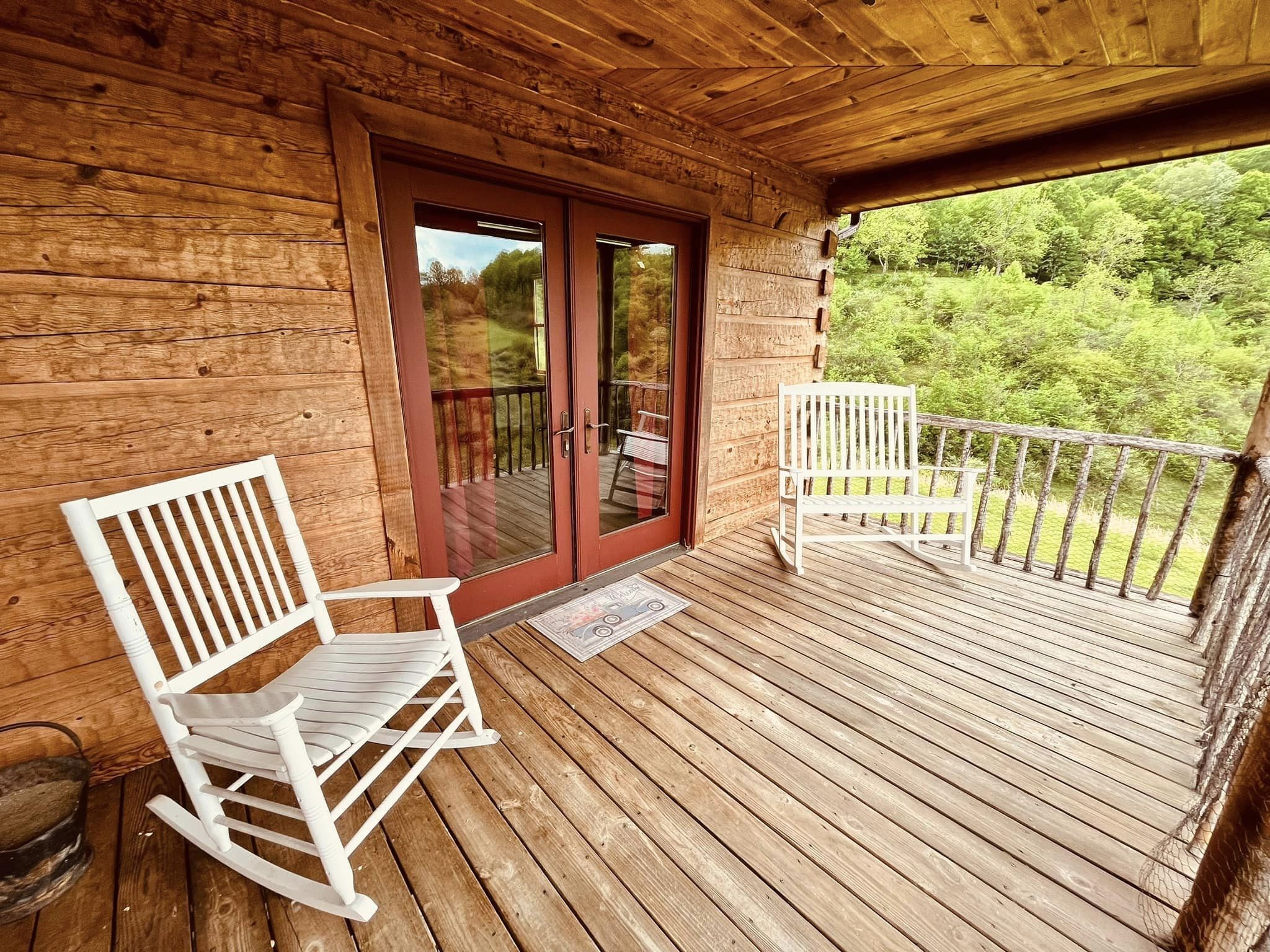 Une terrasse en bois avec deux fauteuils à bascule et une porte vitrée donnant sur un espace extérieur.