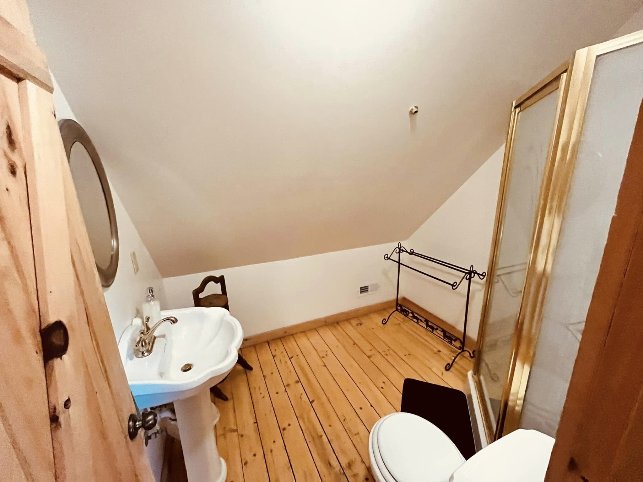 Une petite salle de bain aux dimensions réduites, avec un plancher en bois, un lavabo blanc, des toilettes et une cabine de douche en verre.
