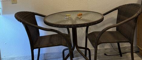 A dining area with a round table and four wicker chairs, a textured wall, and a light switch.