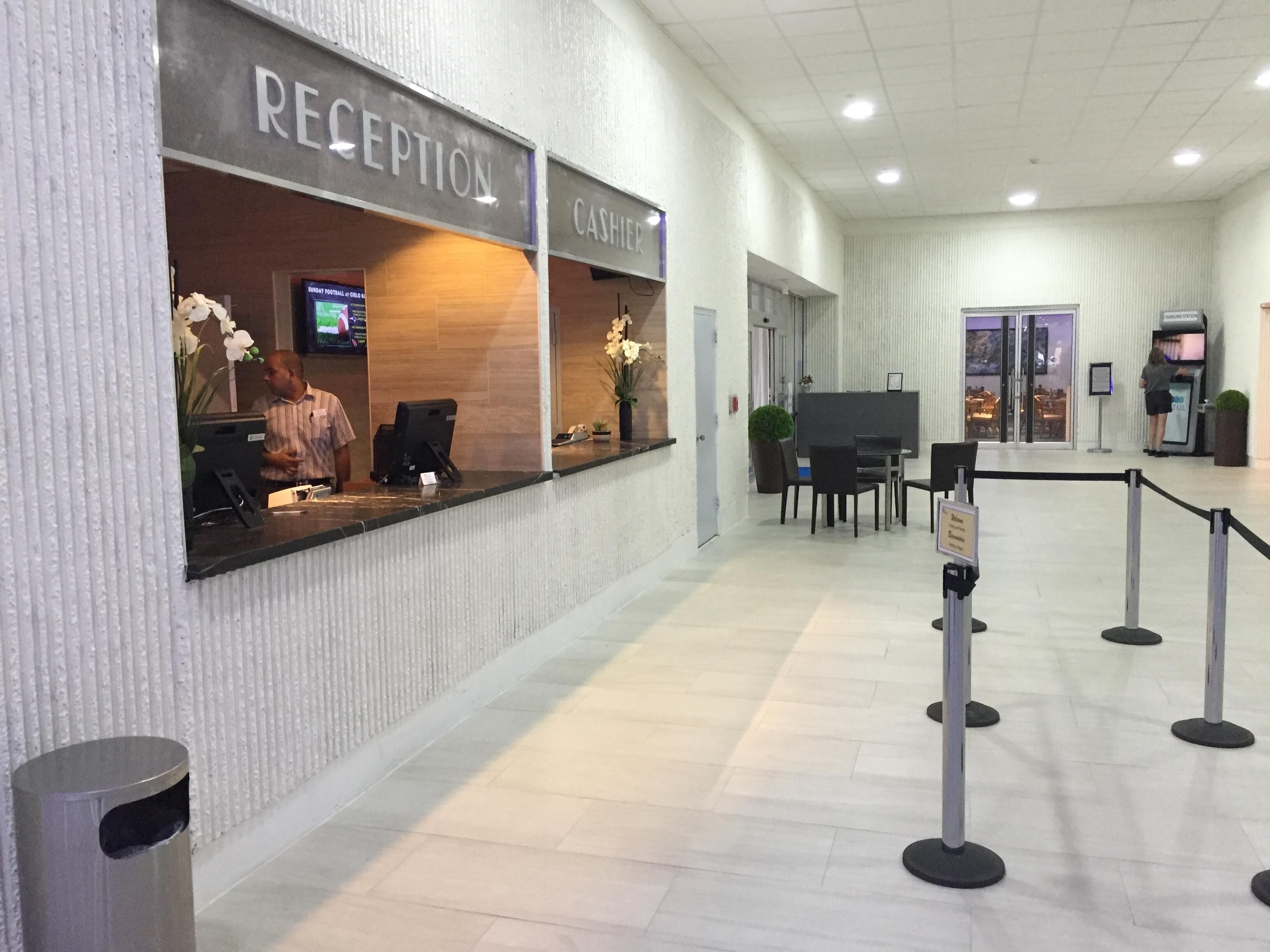 Un espace d’accueil comprenant un comptoir de réception, une caisse et un coin salon avec des tables et des chaises.