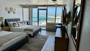 A bedroom with two beds, a large window with a view of the beach, and a balcony.
