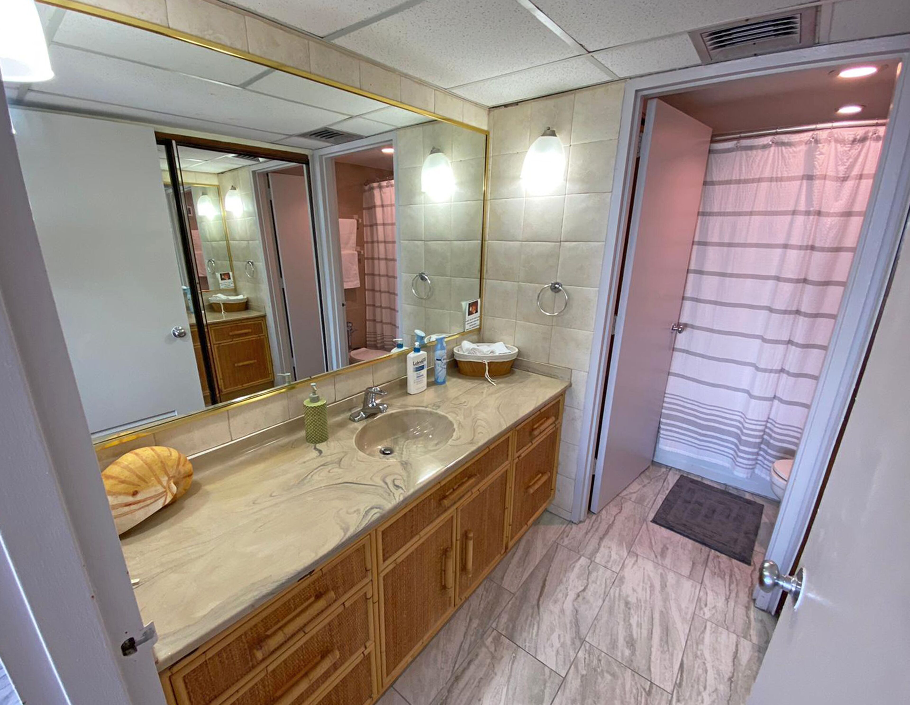 A bathroom with a marble sink, wooden cabinets, a large mirror, and a shower with a striped curtain.