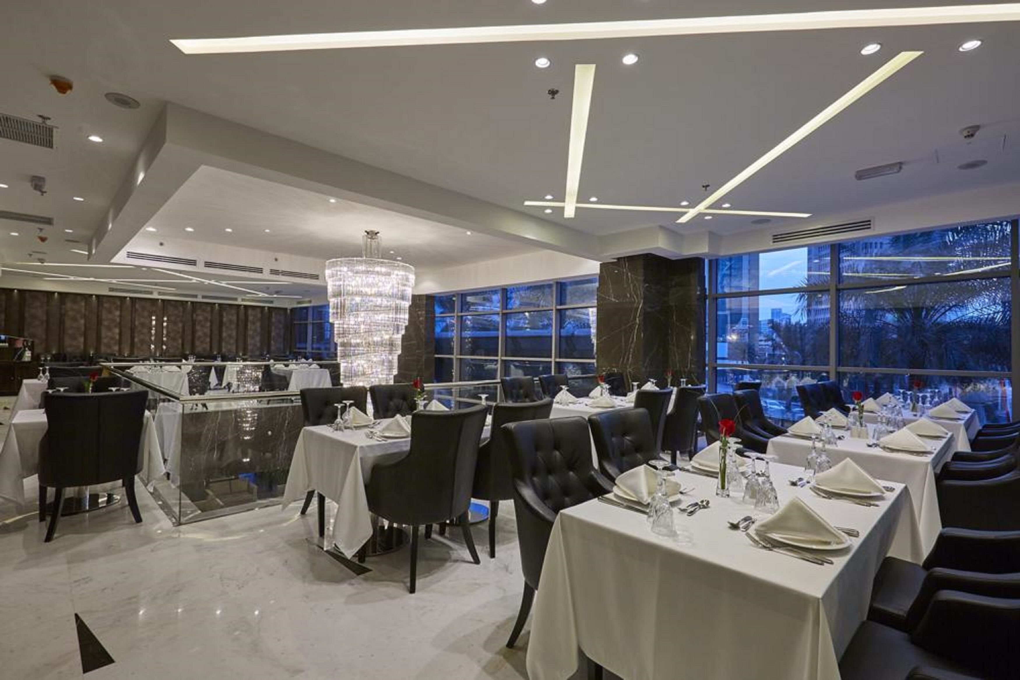 Un restaurant moderne avec des nappes blanches, des chaises noires et un grand lustre.