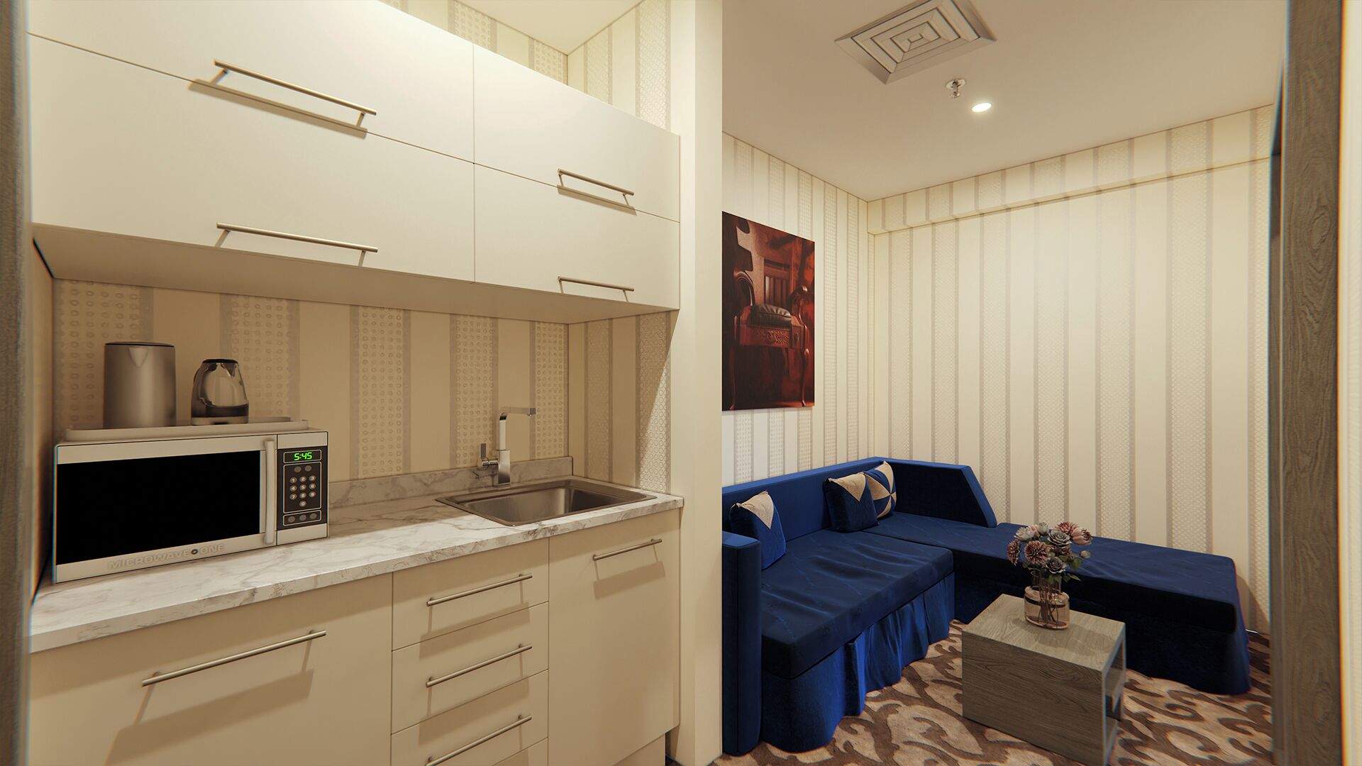 Cocina compacta con microondas, hervidor y lavabo. En la sala de estar, un sofá azul y una pequeña mesa con un florero.