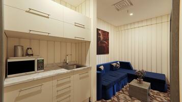 Cocina compacta con microondas, hervidor y lavabo. En la sala de estar, un sofá azul y una pequeña mesa con un florero.