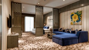 Une chambre d’hôtel moderne dotée d’un grand canapé, d’un coin salon plus petit, d’une télévision et d’un mur décoratif orné d’un tableau floral.