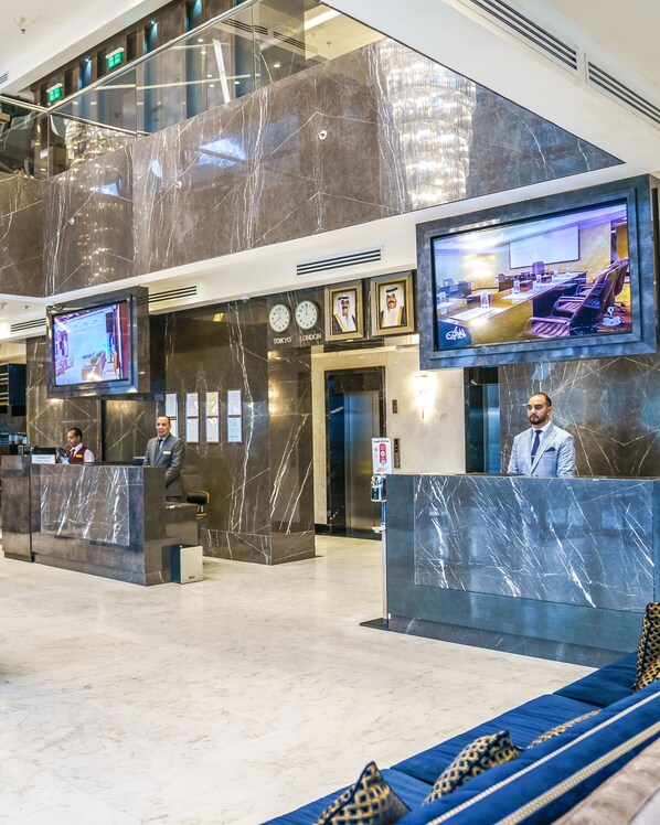 Un vestíbulo con paredes de mármol, un mostrador de recepción, una zona de estar y una pantalla grande que muestra una escena de restaurante.
