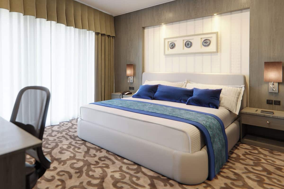 Une chambre d’hôtel avec un grand lit, un bureau et une chaise. Il y a deux tables de chevet avec des lampes.