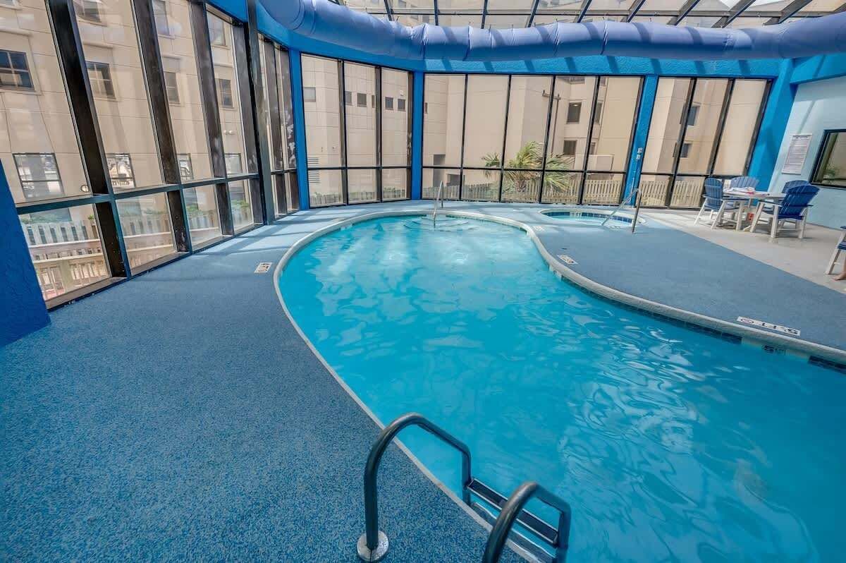 Una piscina interna con acqua cristallina e blu, circondata da ampie vetrate e pavimento blu.