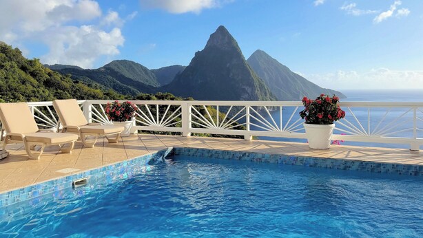 A pool with a view of mountains, lounge chairs, and a railing.