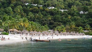 A beach with thatched umbrellas, lounge chairs, and a boat in the water.