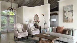 A spacious living room with two armchairs, a sofa, a coffee table, and a large painting on the wall.