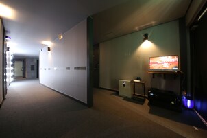 Un pasillo con una televisión de pantalla plana montada en la pared, una mesita pequeña y un calentador en el suelo.