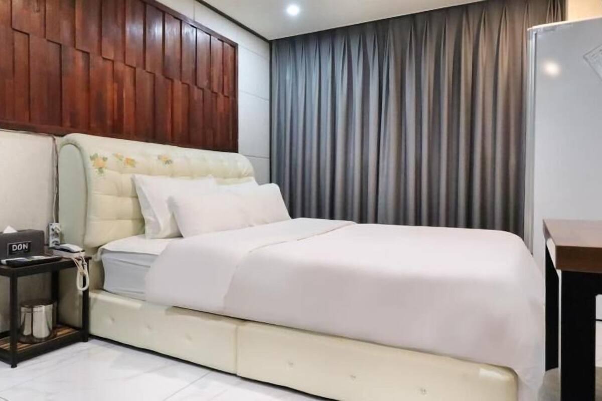 Ein Hotelzimmer mit Bett, Nachttisch, Schreibtisch und Vorhang.