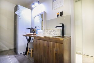 Un baño pequeño con tocador de madera, lavamanos con lavabo estampado, espejo y refrigerador.