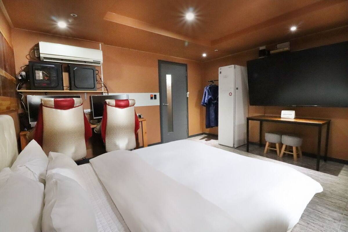 Ein Hotelzimmer mit Bett, zwei Stühlen, einem Schreibtisch, einem Fernseher und einem Kühlschrank.