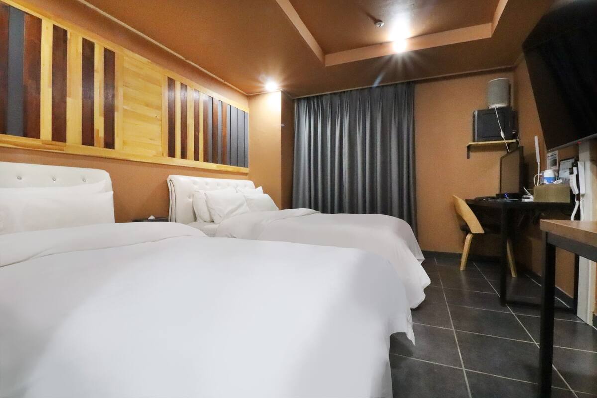 Ein Hotelzimmer mit zwei Betten, einem Schreibtisch, einem Stuhl, einem Fernseher und einem Vorhang.
