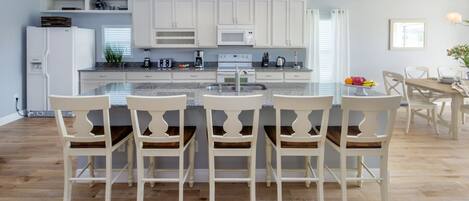 A modern kitchen with white cabinetry, a central island with bar stools, and a dining area with a wooden table and chairs.