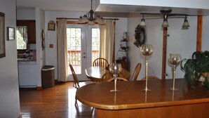 A dining area with a wooden table, chairs, and three wine glasses. A chandelier hangs above the table, and a basket is on the floor. - Lovely cottage in West Asheville. Hot Tub. Pool open for SUMMER! (Asheville)