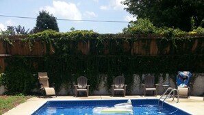 A rectangular swimming pool with clear blue water, surrounded by a wooden fence and chairs. - Lovely cottage in West Asheville. Hot Tub. Pool open for SUMMER! (Asheville)