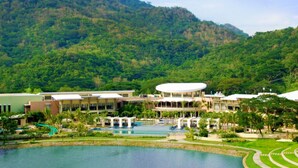 Een resort met meerdere gebouwen, een centraal zwembad en weelderige begroeiing op de achtergrond.