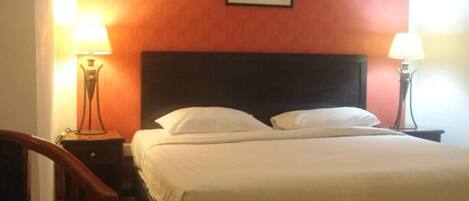 Una habitación de hotel con una cama, dos lámparas de noche, una silla y un cuadro en la pared.