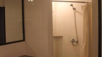 A bathroom with a sink, mirror, shower, and a trash bin.