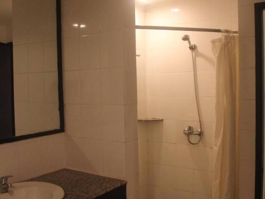 A bathroom with a sink, mirror, shower, and a trash bin.