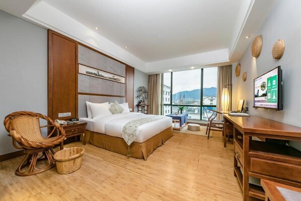 A hotel room with a large bed, a desk, a wicker chair, a TV, and a view of the city. - Fliport Garden Hotel Wuyishan (Nanping)