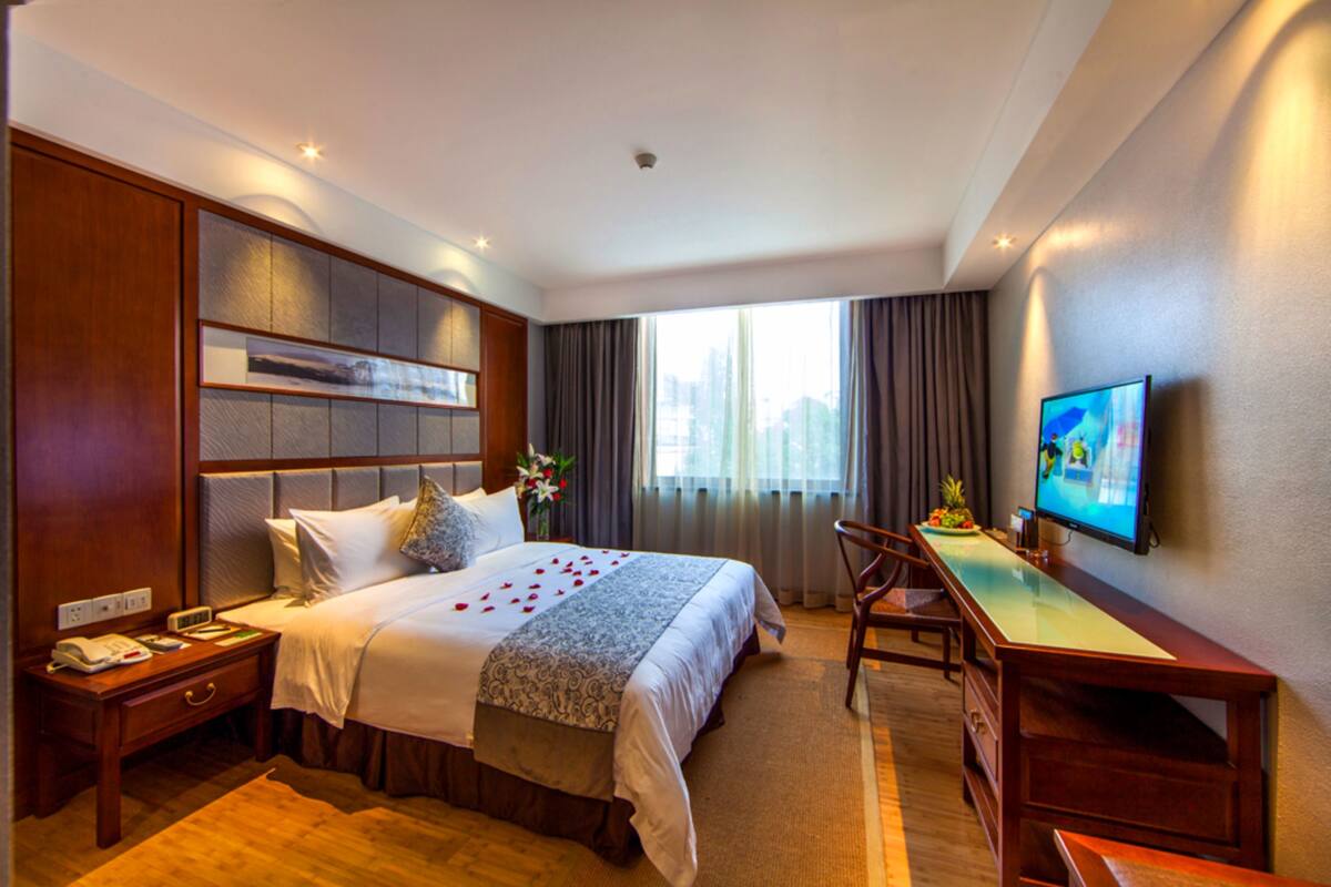 Une chambre d’hôtel avec un grand lit, un bureau, une chaise, une télévision et une fenêtre avec des rideaux.
