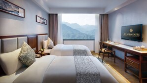 Een hotelkamer met twee bedden, een bureau, een stoel, een televisie en uitzicht op bergen.