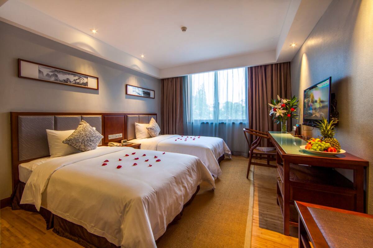 Une chambre d’hôtel avec deux lits, un bureau, une chaise, une télévision et une fenêtre avec des rideaux.