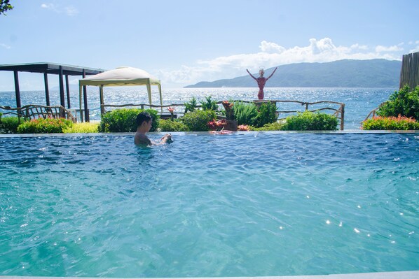 Una piscina con agua cristalina azul, rodeada de exuberante vegetación y una terraza de madera.