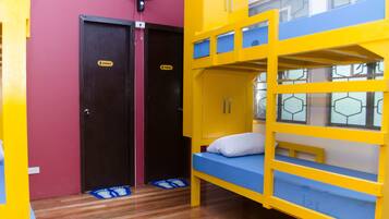 A bunk bed room with a blue mattress and yellow frame, a pair of doors with a 'female' sign, and a fan on the wall.