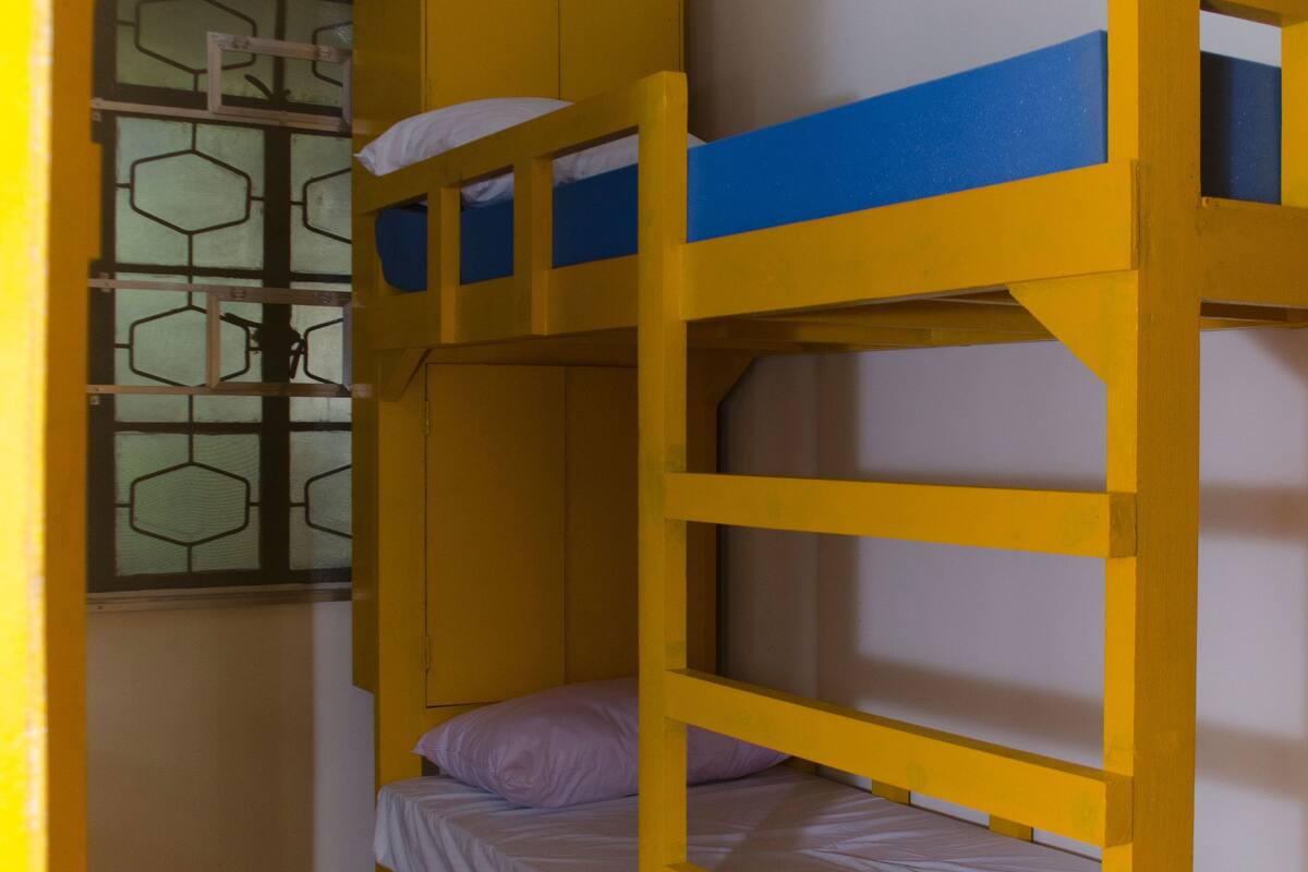 Une chambre avec un lit superposé, une tête de lit jaune et une fenêtre ornée d’un motif géométrique.