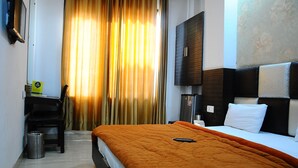A hotel room with a bed, a desk, a chair, a trash bin, and a TV on the wall. - Hotel Winner Inn (Amritsar)
