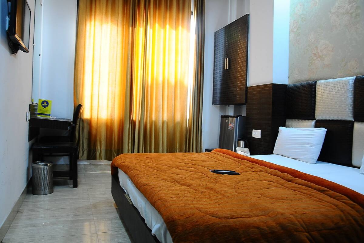 Habitación de hotel con cama, escritorio, silla, cesto de basura y televisión en la pared.