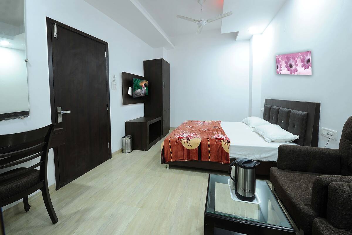 Un dormitorio con cama, televisor, escritorio, silla y sofá.