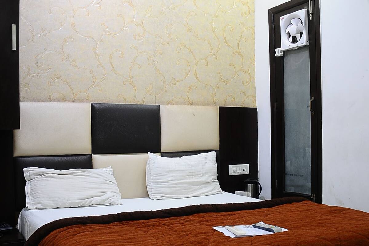 Una cama bien hecha con una colcha marrón, un cabecero con diseño negro y beige, y un aire acondicionado instalado en la pared.