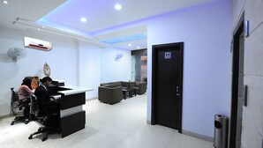 A modern office space with a reception desk, a sofa, and a trash bin. - Hotel Winner Inn (Amritsar)