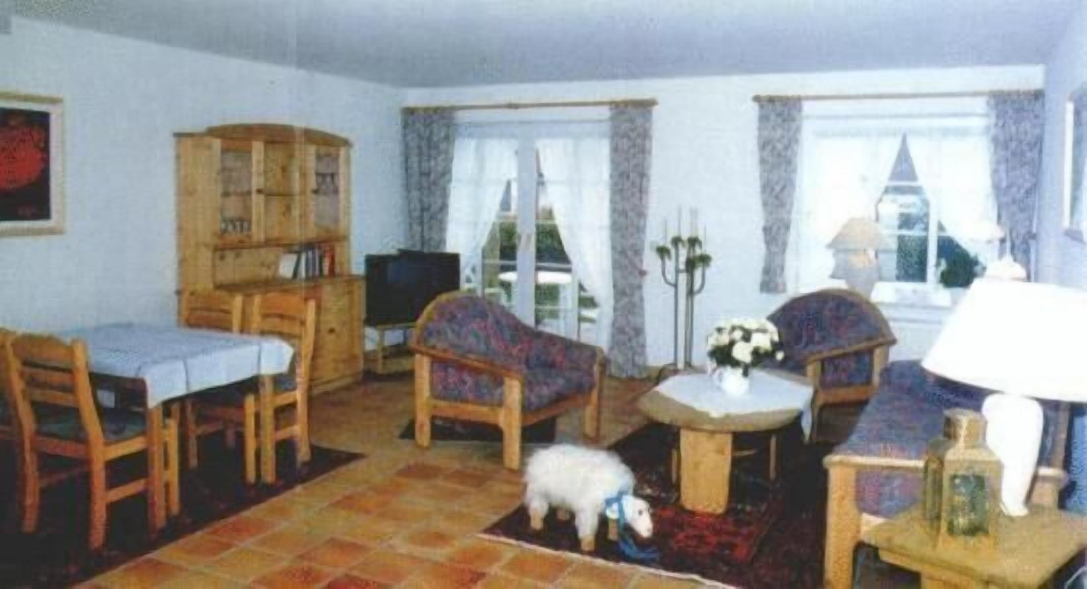 A living room with a sofa, chairs, a small table, a television, and a bookshelf.