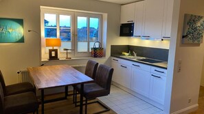 A compact kitchen with a dining table, chairs, a microwave, and cabinets. - Hotel Kiose - Landhaus JOJO (Wenningstedt-Braderup)