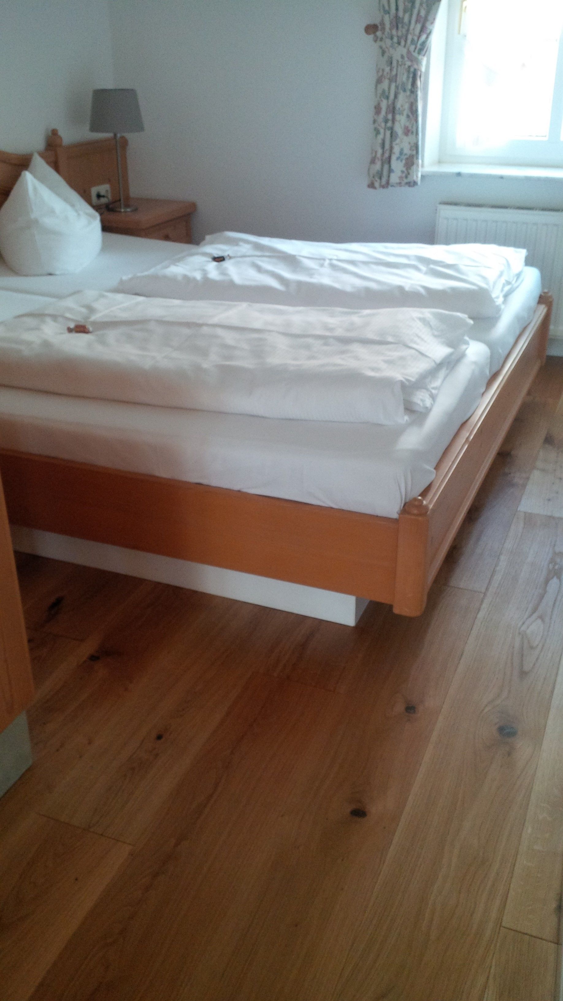 A neatly made bed with white linens in a room with wooden flooring.