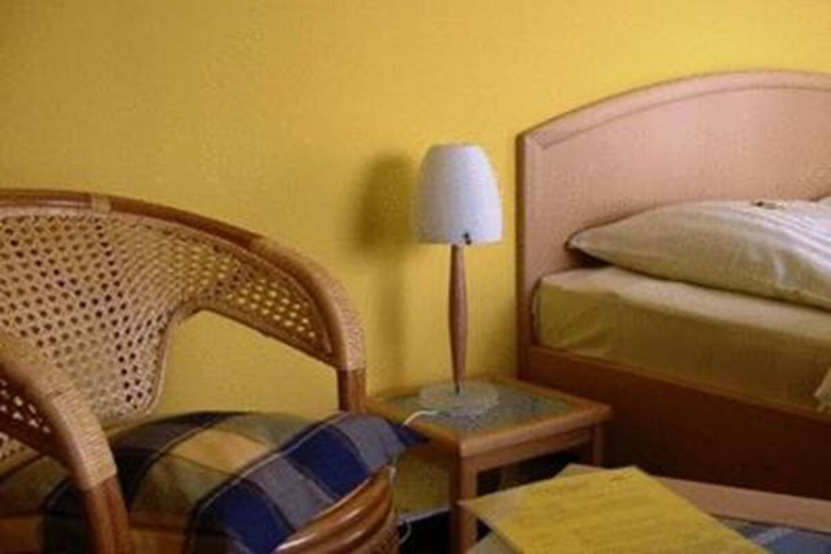 A room with a bed, a nightstand, a lamp, and a wicker chair.