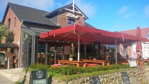 A hotel with a red awning, outdoor seating, and a signboard. - Hotel Kiose - Landhaus JOJO (Wenningstedt-Braderup)