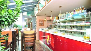 A restaurant with a red counter, glass display cases, and wooden chairs. - Hotel Kiose - Landhaus JOJO (Wenningstedt-Braderup)
